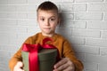 Surprised boy in a yellow sweater holds a green round gift with a red ribbon Royalty Free Stock Photo