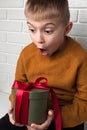 Surprised boy in a yellow sweater holds a green round gift with a red ribbon Royalty Free Stock Photo