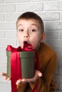 Surprised boy in a yellow sweater holds a green round gift with a red ribbon Royalty Free Stock Photo