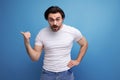 surprised brunette young man in a white t-shirt shows his index finger to the side on a studio background with copyspace Royalty Free Stock Photo