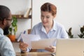 Surprised businesswoman looking at resume of smiling african american candidate