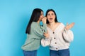 A surprised caucasian woman listens to her twin sister secret. Amazement on blue background