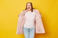 Surprised cheerful brown haired girl wearing pink fur coat with ponytails isolated over yellow background reacts to awesome news