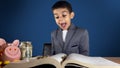 Surprised child boy in a business suit find money while reading a book. blue backgrund with copy space Royalty Free Stock Photo