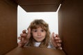 Surprised child boy unpacking, opening carton box and looking inside. Open box and delivery parcel for children