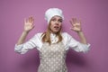 Cook girl in apron raises and shows hands on a pink background, scared woman housewife in kitchen clothes Royalty Free Stock Photo