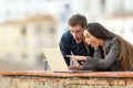 Surprised couple checking laptop content in a balcony