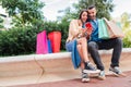 Surprised couple using a cellphone to find sales doing online shopping sitting outside with bags. Man and woman having Royalty Free Stock Photo