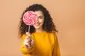 Surprised curly girl eating lollipop. Beauty Model woman holding pink sweet colorful lollipop candy, isolated on beige background Royalty Free Stock Photo