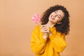 Surprised curly girl eating lollipop. Beauty Model woman holding pink sweet colorful lollipop candy, isolated on beige background Royalty Free Stock Photo