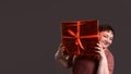 surprised curvy woman holding gift box and hiding behind big red present box on neutral monochrome gray background Royalty Free Stock Photo