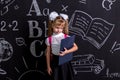Surprised and disappointed schoolgirl standing before the chalkboard as a background with a pink backpack on her back