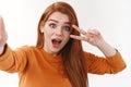 Surprised emotional cute redhead woman in orange sweater, holding camera with extended arm, taking selfie with funny