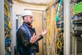 Surprised engineer in white helmet spreads his arms to the side near the rack with server equipment. Messy Internet wires are Royalty Free Stock Photo