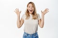 Surprised and excited blond girl screams of joy, reacting amazed and happy at promo sale, super big news, standing over Royalty Free Stock Photo