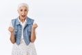 Surprised and excited happy triumphing old woman with grey hair, clench hands, fist pump celebrating win, won lottery Royalty Free Stock Photo