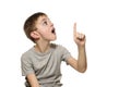Surprised fair-haired boy in a gray T-shirt stands and points with the index fingers up. Isolate on white background