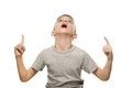 Surprised fair-haired boy in a gray T-shirt stands and points with the index fingers up. Isolate on white background