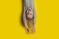 Surprised fair-haired boy hanging upside down with arms outstretched. Portrait of child on bright yellow background