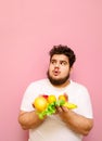 Surprised fat man on diet standing with fruits in hands on pink background and looking up at copy space with shocked face. Royalty Free Stock Photo