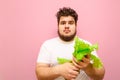 Surprised fat man isolated on pink background with lettuce in his hands, looks into camera with shocked face. Emotional overweight Royalty Free Stock Photo