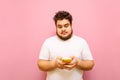 Surprised fat man uses smartphone on pink background, looks into screen with shocked face. Funny bearded guy with overweight and Royalty Free Stock Photo
