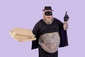 Surprised fat man in Zorro costume holds pizzas and points up on purple background Royalty Free Stock Photo