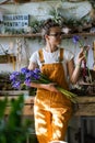 Surprised florist woman surrounded by collection of tillandsia air plants, smiling, looking at a bouquet of irises flowers. Indoor
