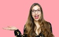 Surprised funny model girl wearing glasses and showing on open hand palm for text on pink background. Happy girl presenting