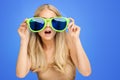 Surprised Girl in Big Party Glasses over Blue Background. Shocked Young Woman looking through Sunglasses. Portrait of Funny Girl Royalty Free Stock Photo