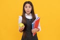 Surprised girl child hold apple and school textbooks yellow background, homework Royalty Free Stock Photo