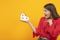 Surprised girl holds model of house on palm on bright orange background. Winning apartment. Real estate as gift