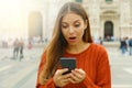 Surprised girl looks at mobile phone in city square in autumn