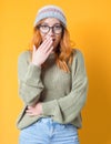 Surprised girl looks to camera  isolated on yellow background. Cheerful young woman covering her mouth with hand Royalty Free Stock Photo