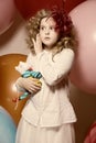 Surprised girl with a soft toy surrounded by huge balloons