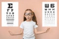 Surprised girl 7 years old in round glasses against the background of blurry tables for checking visual acuity Royalty Free Stock Photo