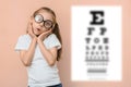 Surprised girl 5 - 7 years old in round glasses on the background of a blurred snellen table for checking visual acuity Royalty Free Stock Photo