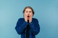 Surprised guy in casual clothes stands on a blue background and putting his hands to his face emotionally looks at the camera and Royalty Free Stock Photo