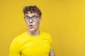 Surprised guy student with curly hair holding glasses and looking at copy space, nerd in glasses on yellow background Royalty Free Stock Photo