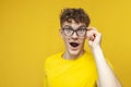 Surprised guy student with curly hair holding glasses and looking, cute nerd in glasses on yellow background Royalty Free Stock Photo