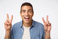 Surprised, handsome masculine young hispanic guy in shirt over t-shirt. showing peace or quotation gesture, smiling Royalty Free Stock Photo