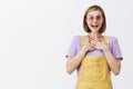 Surprised and happy beautiful young female florist in yellow overalls and pink sunglasses, holding palms on chest and Royalty Free Stock Photo