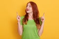 Surprised happy red haired girl in casual green t shirt looking astonished and pointing up with forefingers, posing isolated over Royalty Free Stock Photo