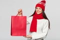 Surprised happy woman holding red bag in excitement, shopping. Christmas girl on winter sale with gift, isolated on gray