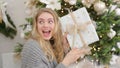 Surprised and happy young woman with christmas present box near christmas tree. Royalty Free Stock Photo