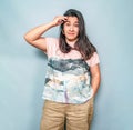 Surprised hispanic woman with dark hair. She holds her hand near head. Posing on gray background