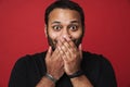 Surprised indian man covering his mouth isolated over red wall