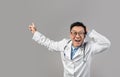 Surprised inspired mature chinese man doctor in white coat, glasses with open mouth pointing finger at free space