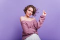 Surprised lady in stylish pink shoes standing on one leg and pointing finger. Indoor photo of cute curly girl in sweater