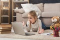 Surprised little girl doing homework on laptop, lying on floor